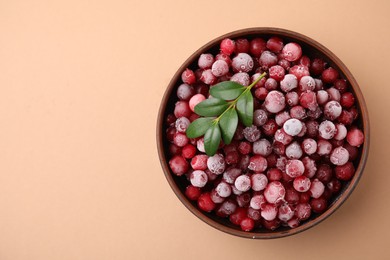 Frozen red cranberries and green leaves on beige background, top view. Space for text