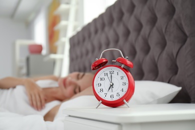 Analog alarm clock and blurred sleepy woman on background. Time of day