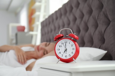 Photo of Analog alarm clock and blurred sleepy woman on background. Time of day