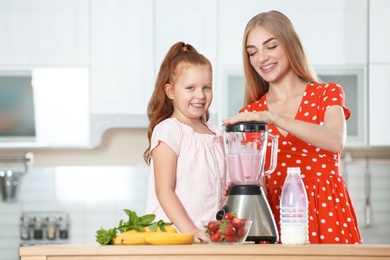 Photo of Mother and daughter preparing delicious milk shake in kitchen