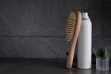 Photo of Dry shampoo spray, eucalyptus branch and hairbrush on dark table near grey wall. Space for text
