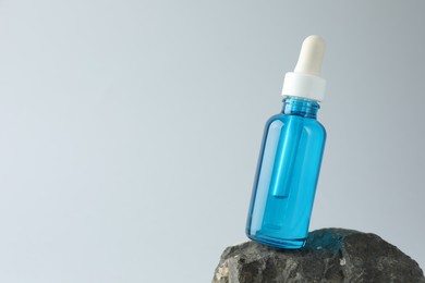 Bottle of cosmetic serum on stone against light grey background, space for text