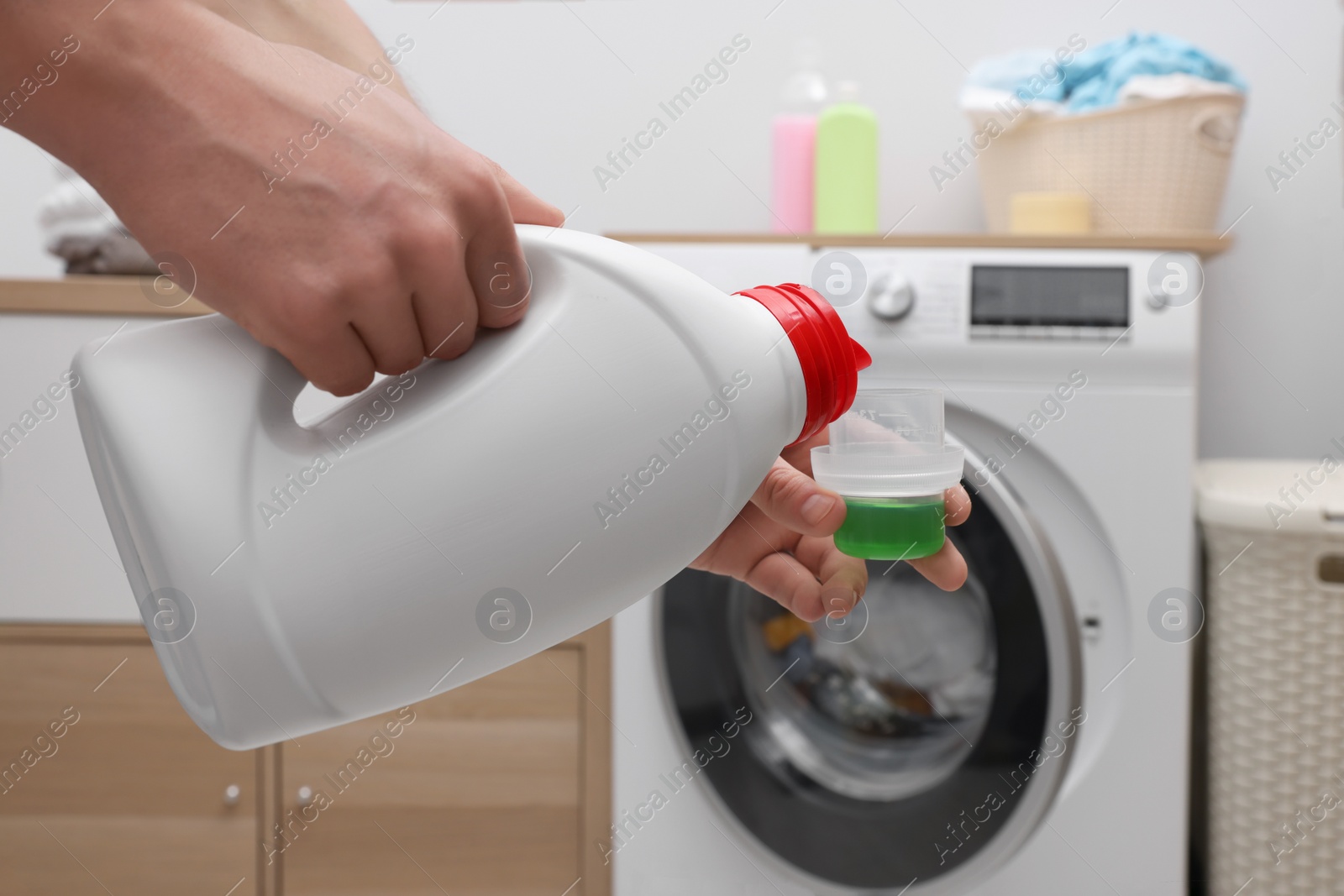Man pouring fabric softener from bottle into cap near washing machine indoors, closeup Photo of Man pouring fabric softener from bottle into cap near washing machine indoors, closeup