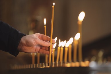 Photo of Man putting candle on stand in church, closeup. Baptism ceremony