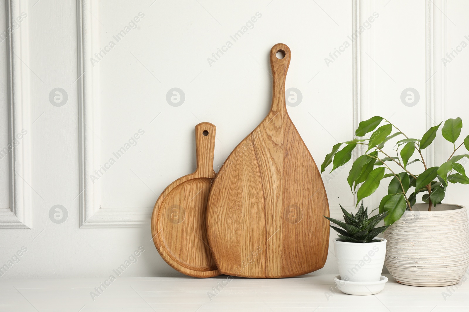 Photo of Wooden cutting boards and houseplants on white table, space for text