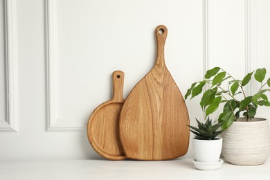 Photo of Wooden cutting boards and houseplants on white table, space for text