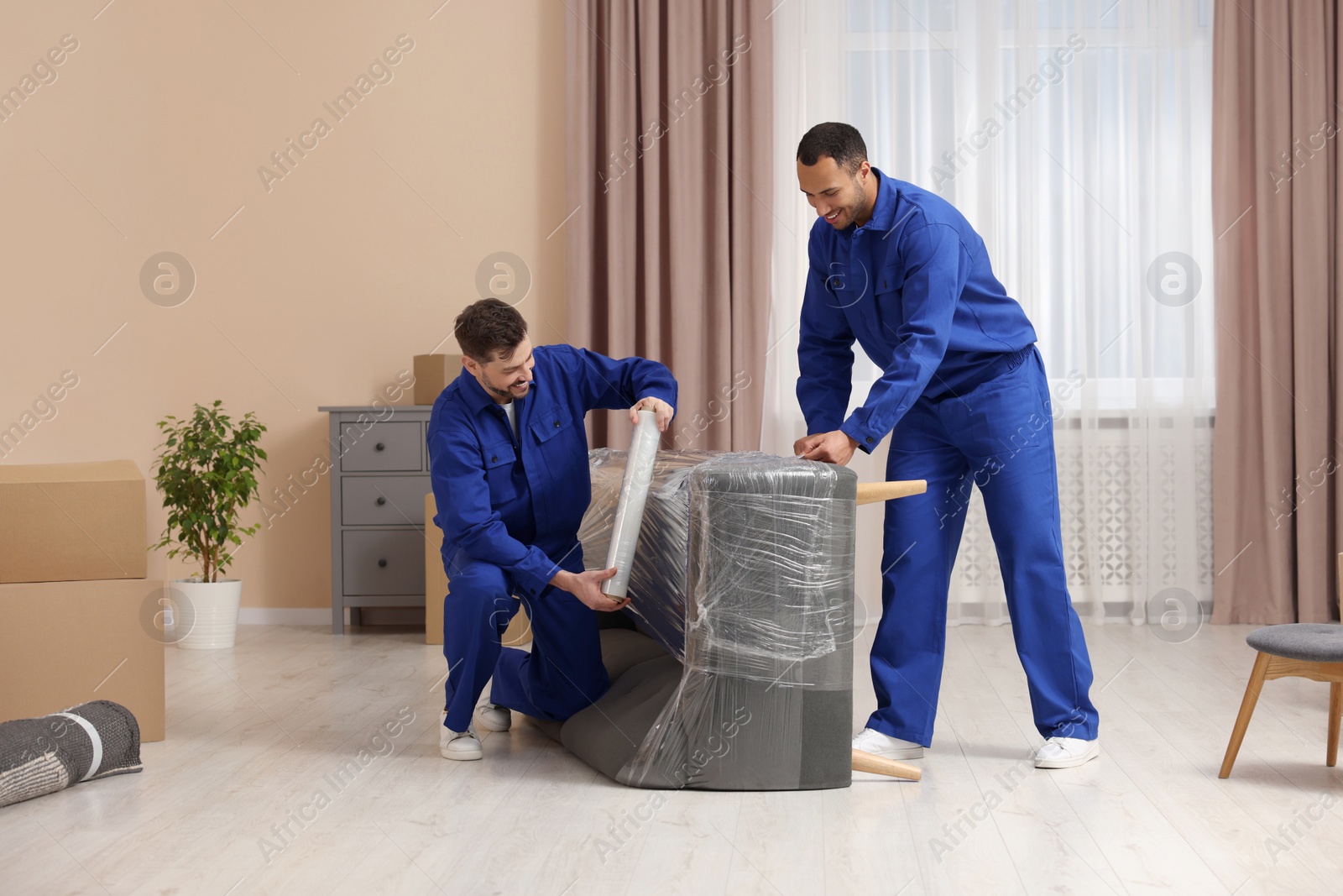 Photo of Male movers with stretch film wrapping sofa in new house