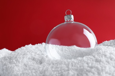 Photo of Transparent Christmas ball on snow against red background, space for text