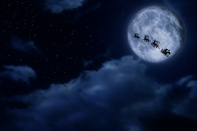 Image of Magic Christmas eve. Santa with reindeers flying in sky on full moon night