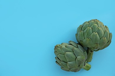 Photo of Whole fresh raw artichokes on light blue background, flat lay. Space for text