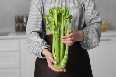 Woman with fresh green celery in kitchen, closeup