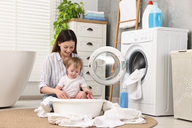 Photo of Happy mother with her daughter having fun while washing baby clothes in bathroom