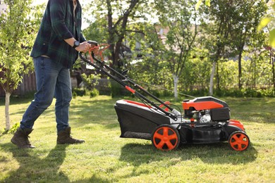 Photo of Man cutting green grass with lawn mower in garden, closeup