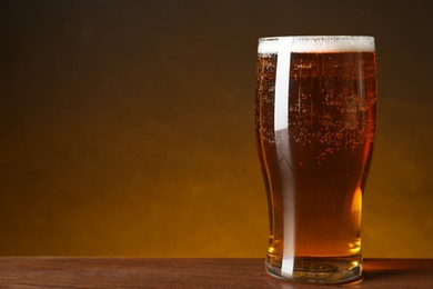 Photo of Glass with fresh beer on wooden table against dark background, closeup. Space for text