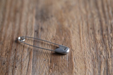 New safety pin on wooden table, closeup. Space for text