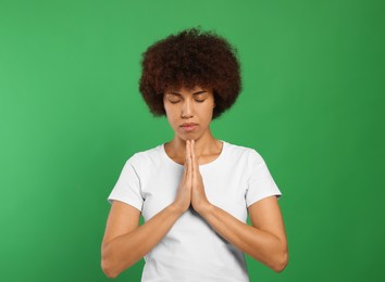 Woman with clasped hands praying to God on green background