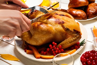 Woman eating traditional cooked turkey at white wooden table, closeup. Thanksgiving day celebration