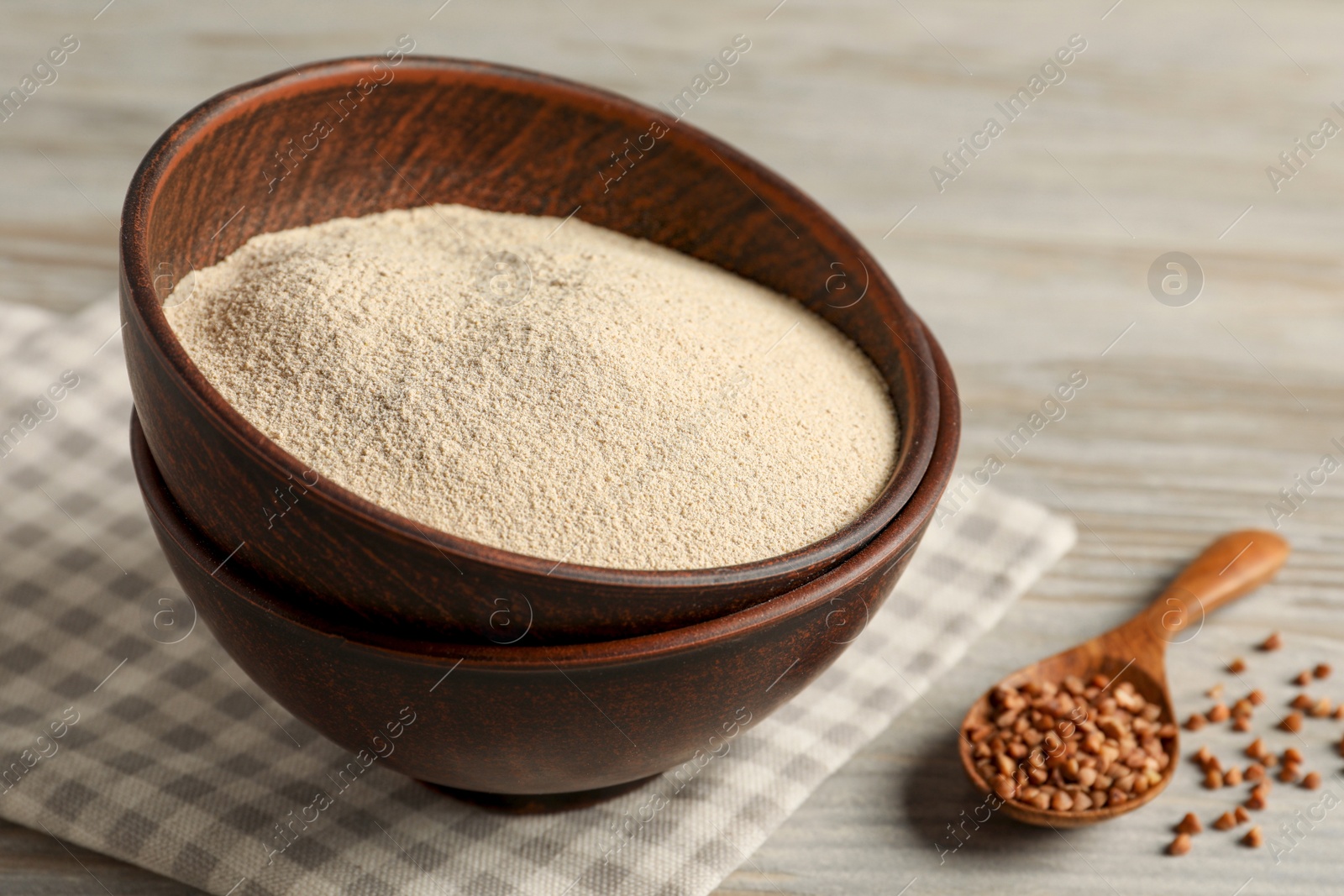 Photo of Bowl with buckwheat flour and seeds on light wooden table, space for text