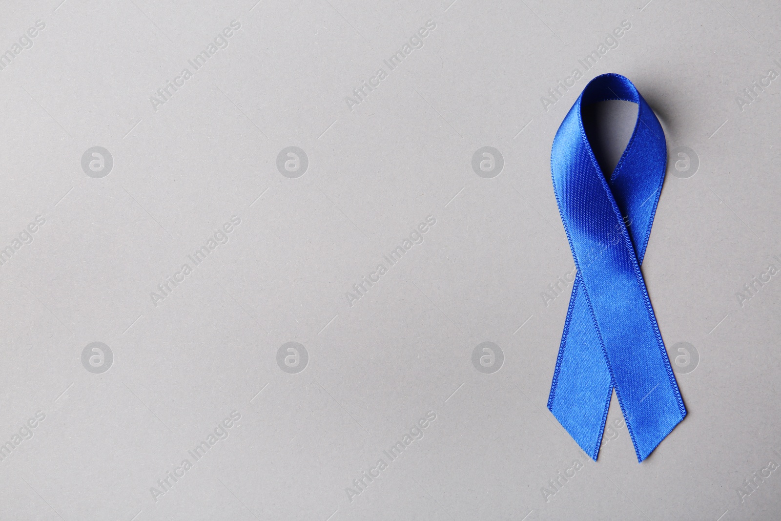 Photo of Blue ribbon on color background, top view with space for text. Colon cancer awareness concept