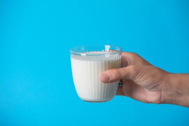 Woman holding fresh milk in glass on light blue background, closeup