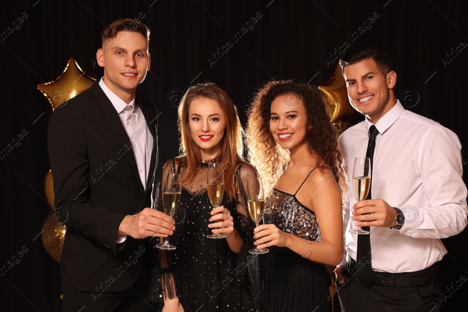 Photo of Happy friends with glasses of sparkling wine celebrating New Year on black background