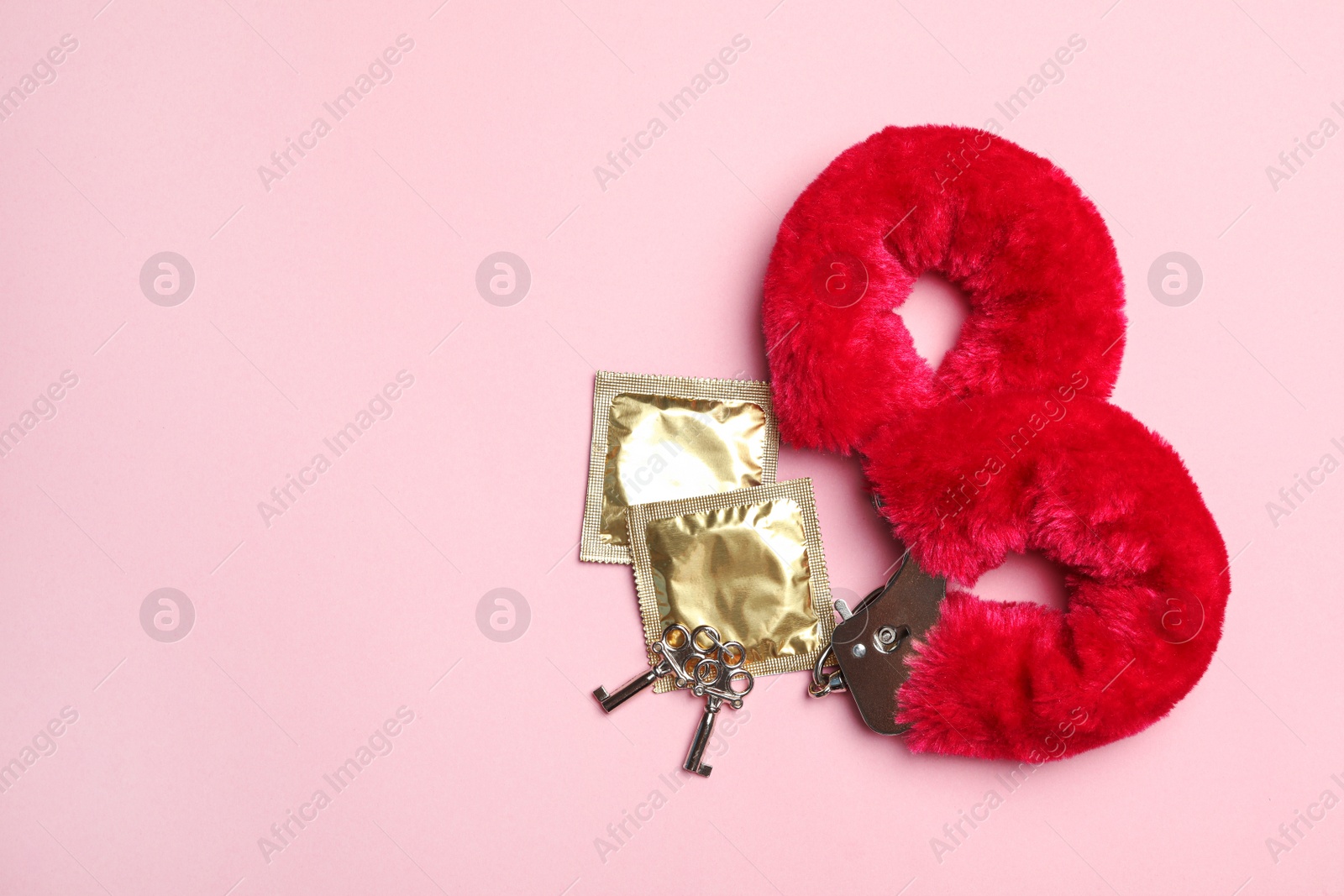 Photo of Furry handcuffs and condoms on pink background, top view with space for text. Sex game