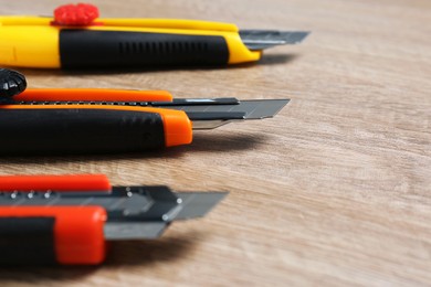 Photo of Three utility knives on wooden table, closeup. Space for text