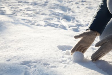 Woman rolling snowball outdoors on winter day, closeup. Space for text