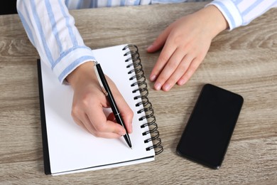 Photo of Woman writing in notebook at wooden table, above view