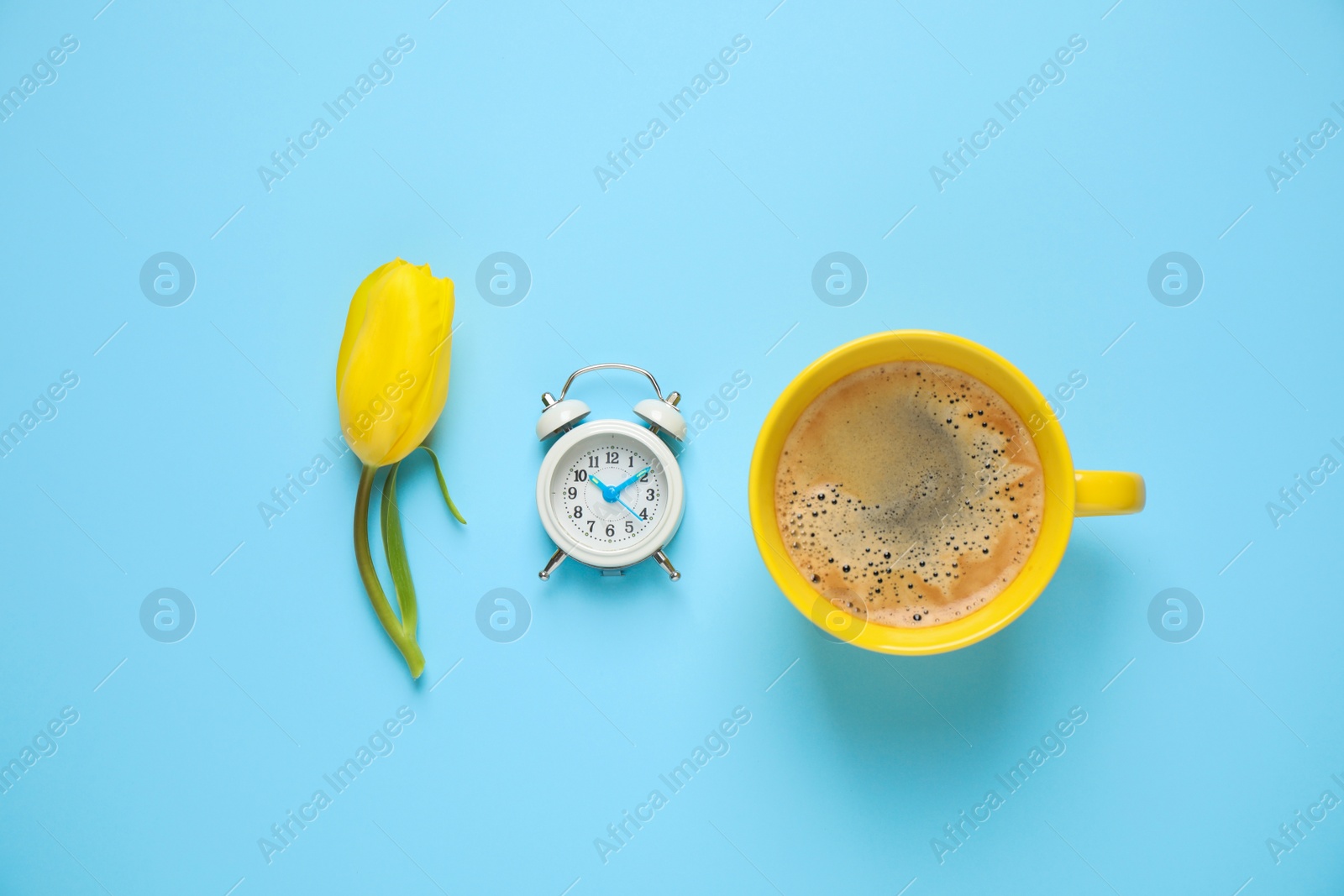 Photo of Delicious morning coffee, alarm clock and tulip on light blue background, flat lay