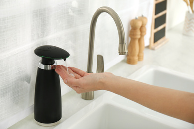 Woman using automatic soap dispenser in kitchen, closeup