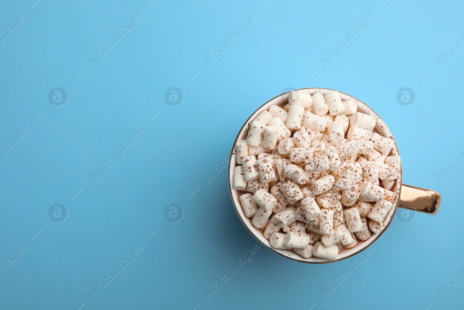 Photo of Delicious cocoa drink with marshmallows on light blue background, top view. Space for text