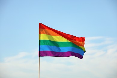Photo of Bright LGBT flag against blue sky with clouds