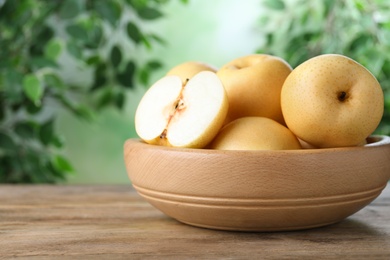 Photo of Cut and whole apple pears in bowl on wooden table against blurred background
