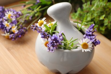 Mortar with fresh lavender, chamomile flowers, rosemary and pestle on wooden table