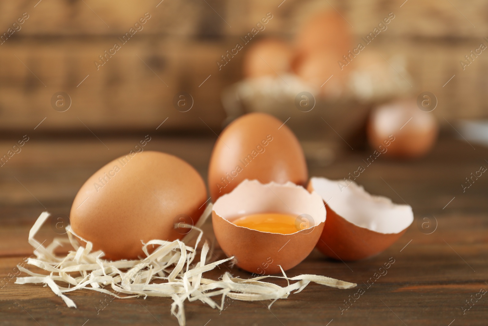 Photo of Raw brown chicken eggs and decorative straw on wooden table