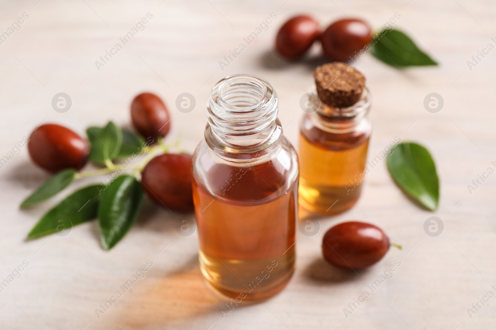 Photo of Glass bottles with jojoba oil and seeds on light table