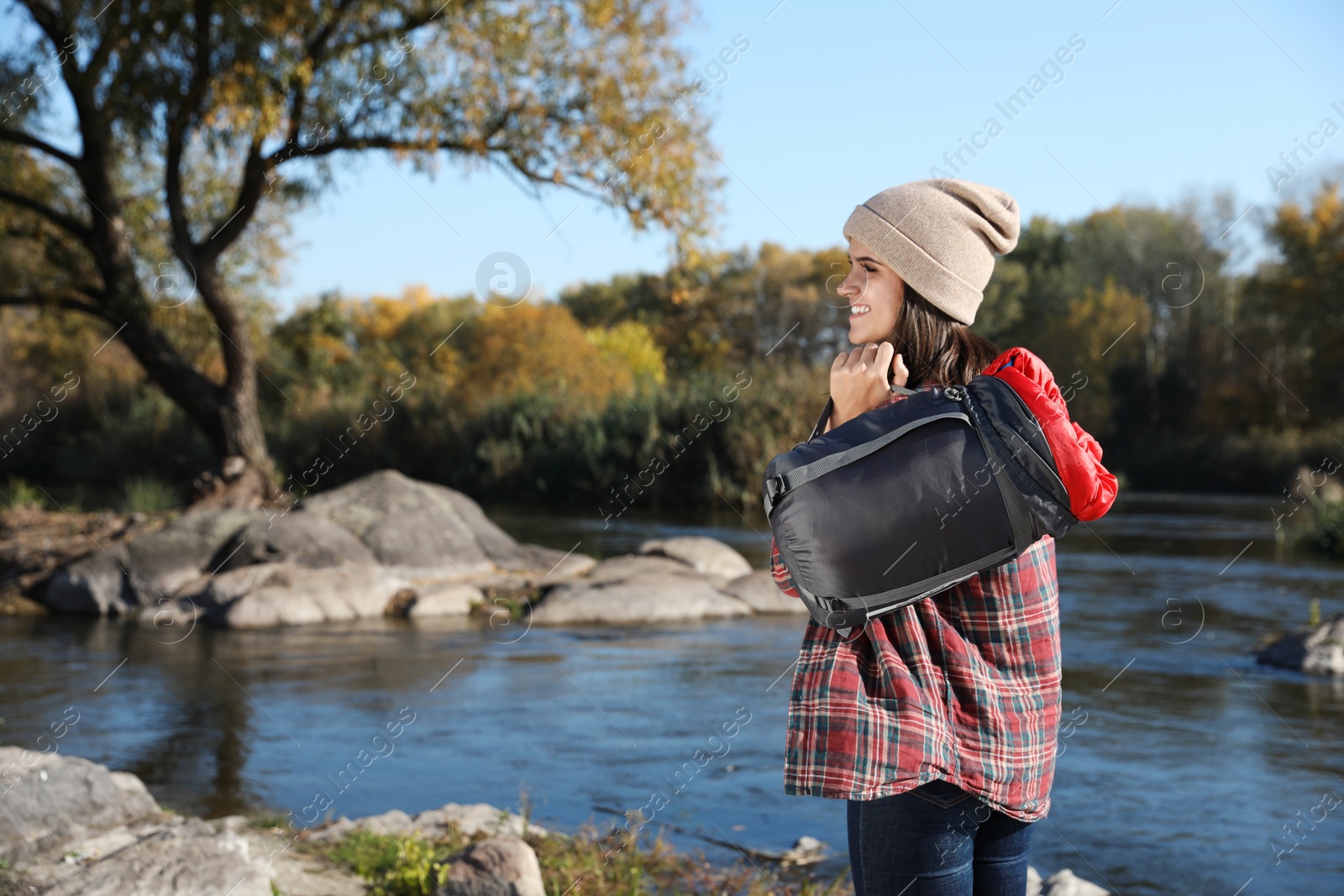 Photo of Female camper with sleeping bag near pond. Space for text