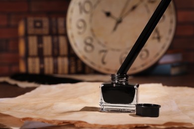 Photo of Inkwell with fountain pen and vintage parchment on table. Space for text