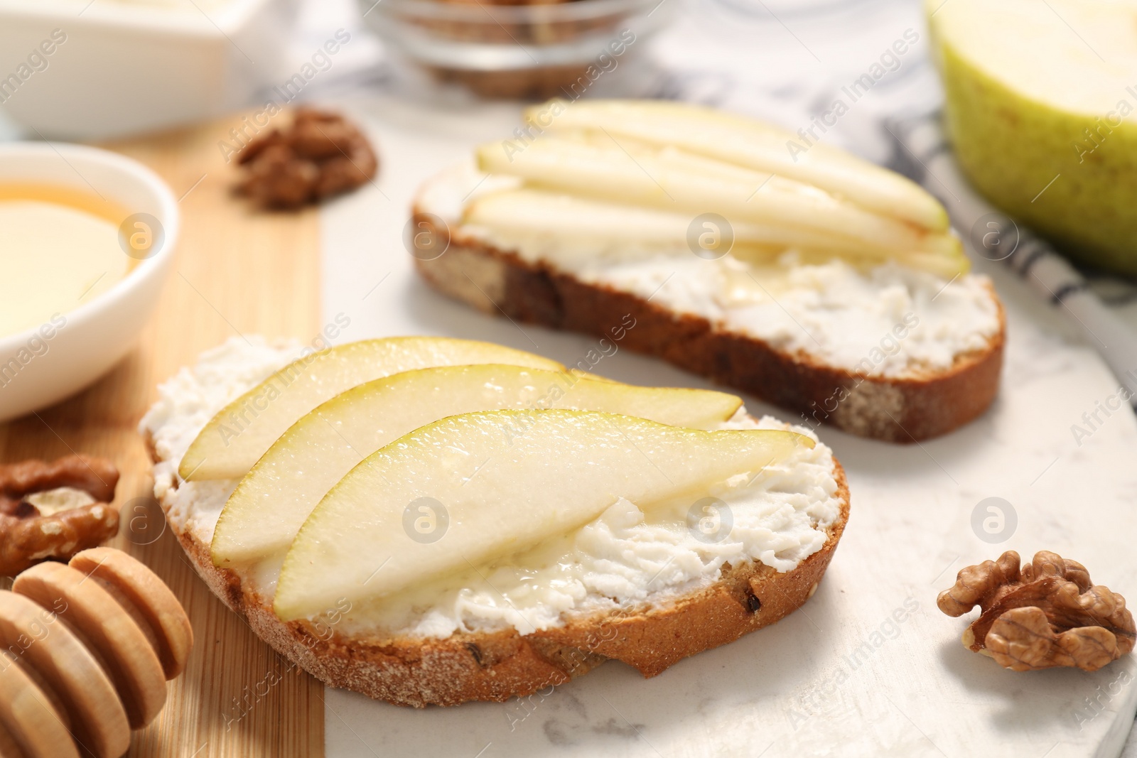 Photo of Delicious ricotta bruschettas with pear and walnut on white table, closeup