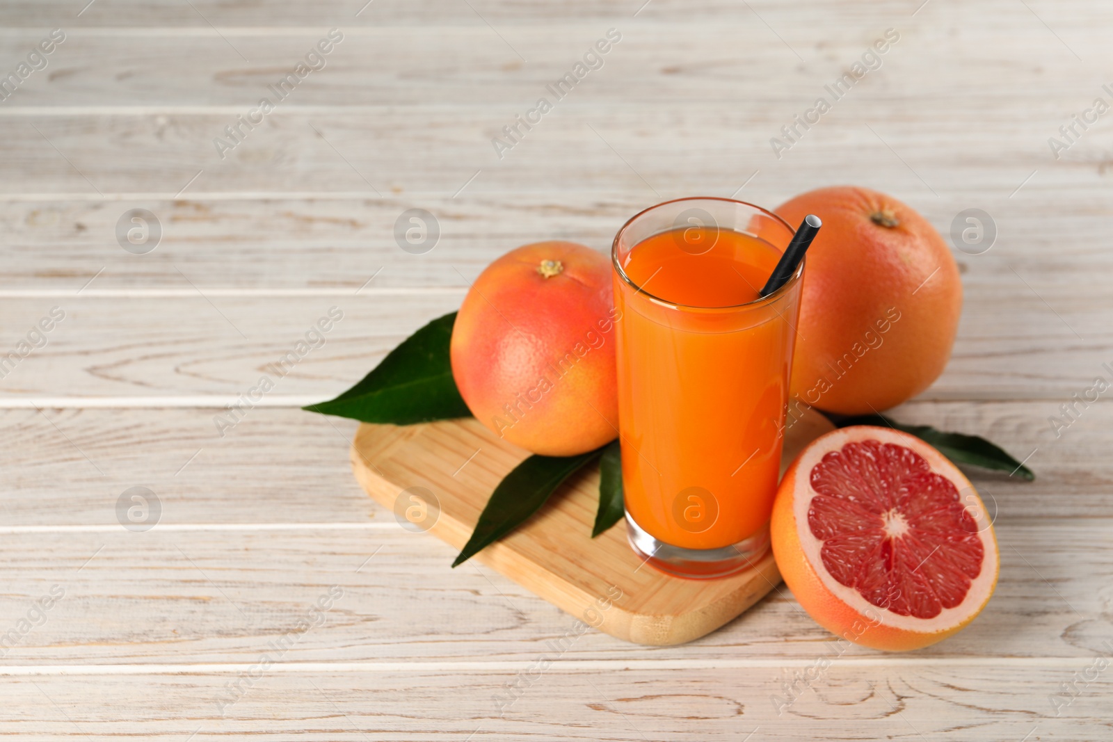 Photo of Tasty grapefruit juice in glass and fresh fruits on light wooden table. Space for text