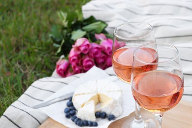 Glasses of delicious rose wine, flowers and food on picnic blanket outdoors