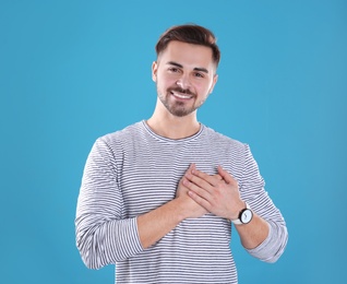 Portrait of young man holding hands near heart on color background