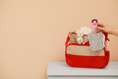 Photo of Woman putting empty nibbler into mother`s bag at white table near beige wall, closeup. Space for text