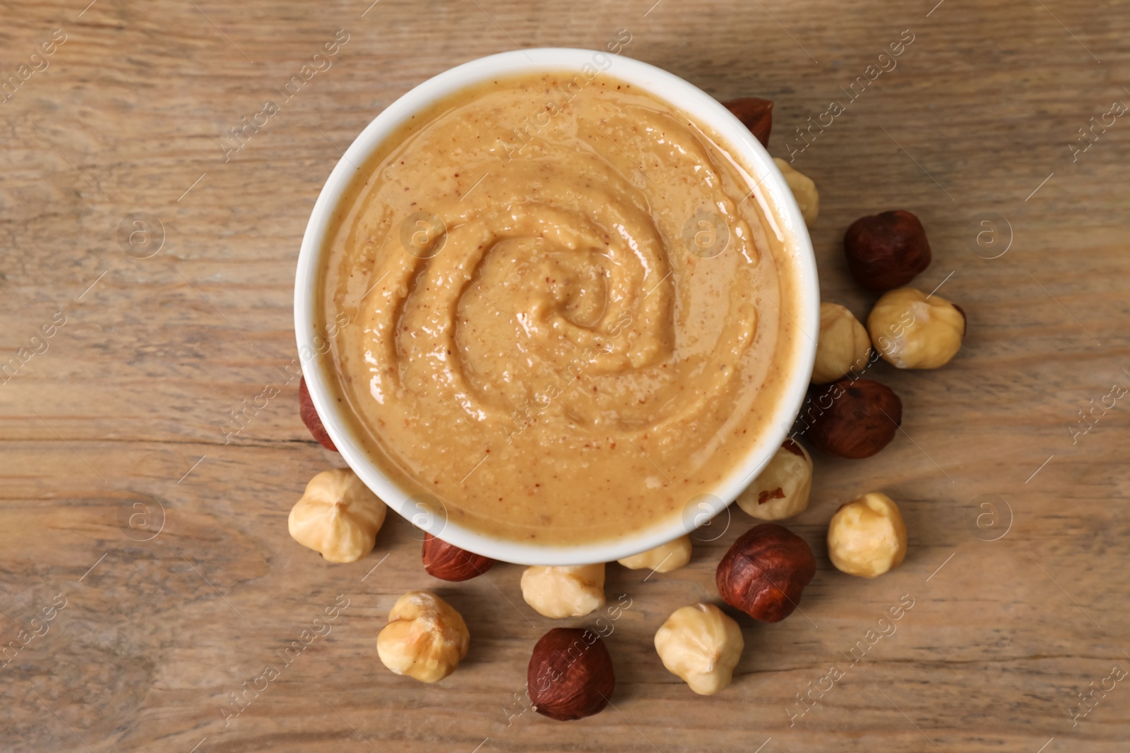 Photo of Delicious nut butter in bowl and hazelnuts on wooden table, top view