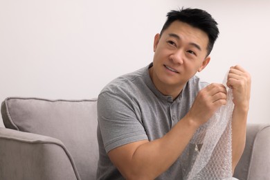 Photo of Asian man with bubble wrap indoors. Space for text