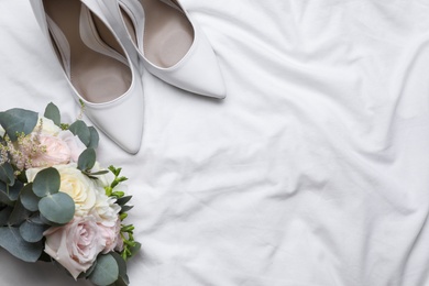 Photo of Pair of wedding high heel shoes and beautiful bouquet on white fabric, flat lay. Space for text
