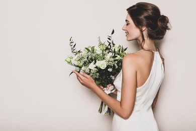 Young bride wearing wedding dress with beautiful bouquet on beige background