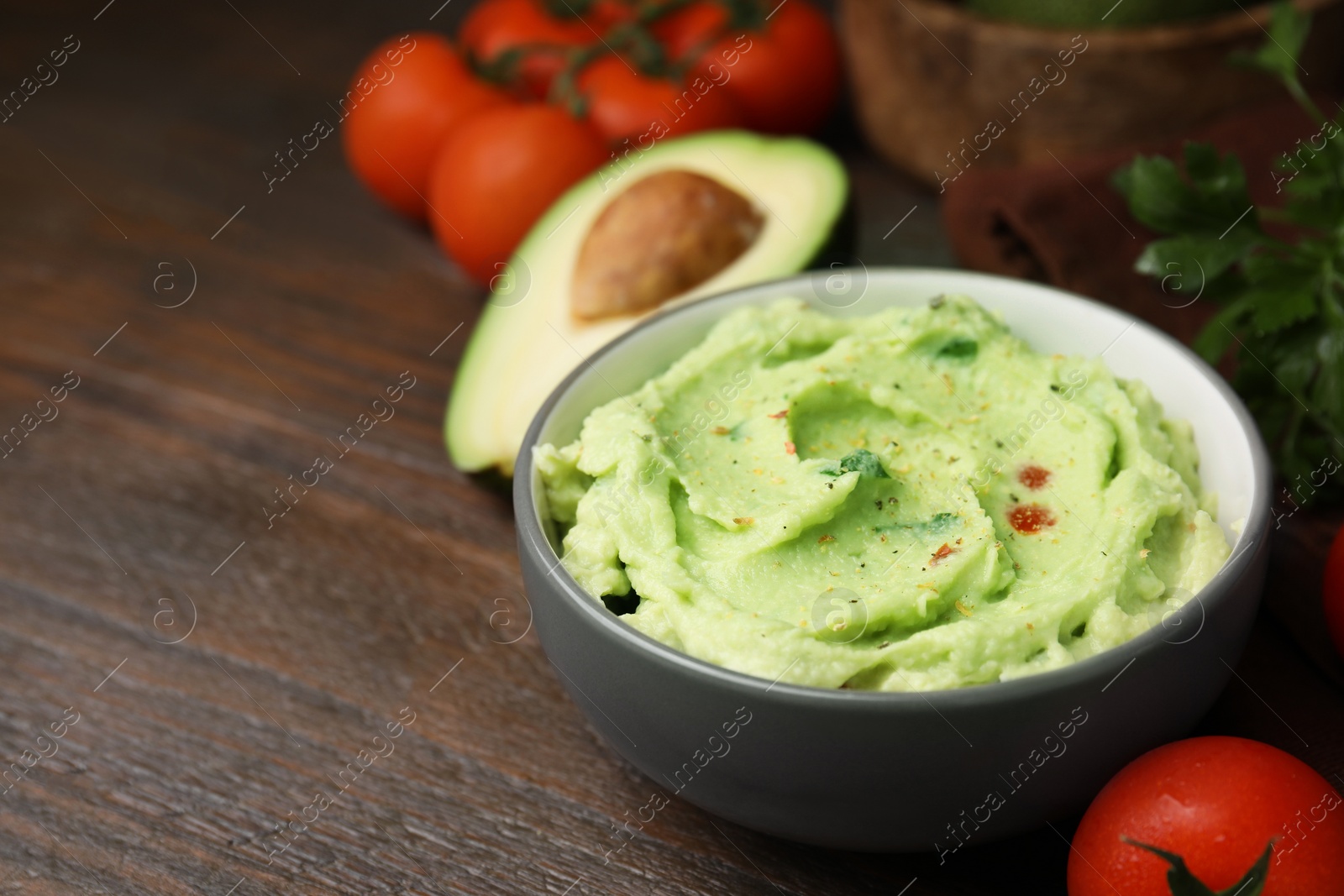 Photo of Bowl of delicious guacamole and ingredients on wooden table. Space for text