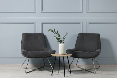 Photo of Comfortable armchairs, side table and eucalyptus indoors